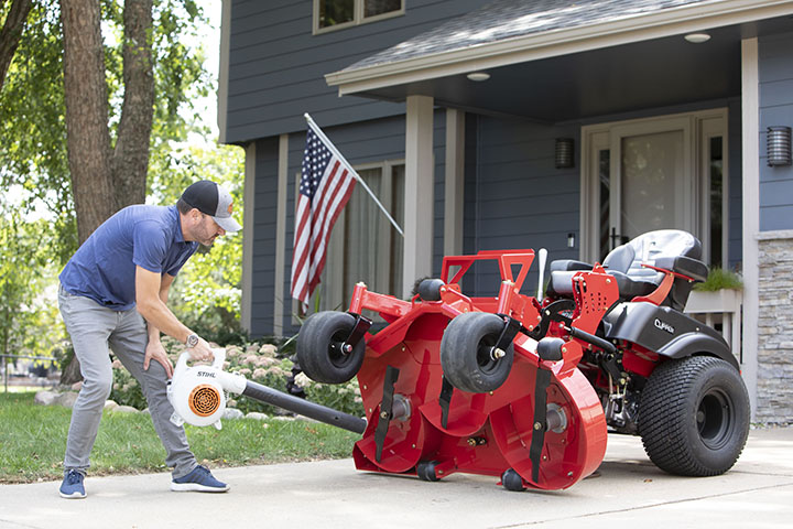 Guy cleaning the underside of a Country Clipper zero turn mower deck using the stand-up deck feature.