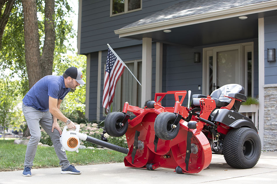 Guy cleaning the underside of a Country Clipper zero turn mower deck using the Stand-Up Deck feature.