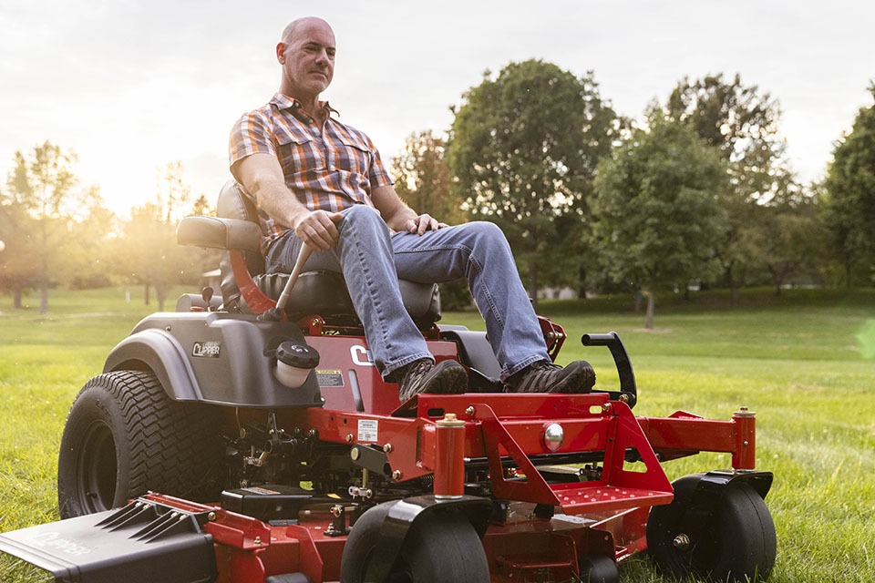 Guy mowing with a Country Clipper zero-turn mower with joystick steering.